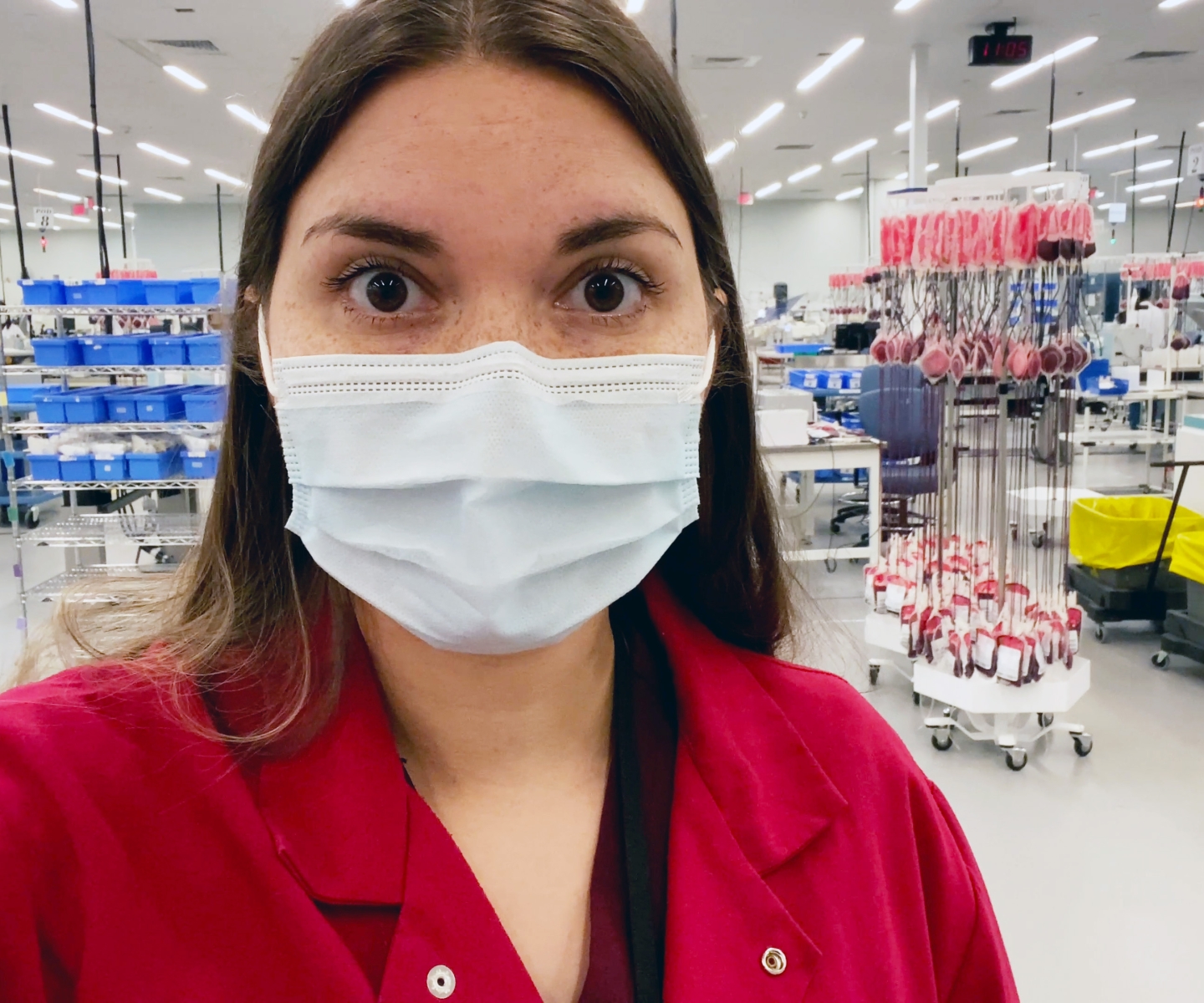 Doctor in red lab coat front of equipment at blood production facility