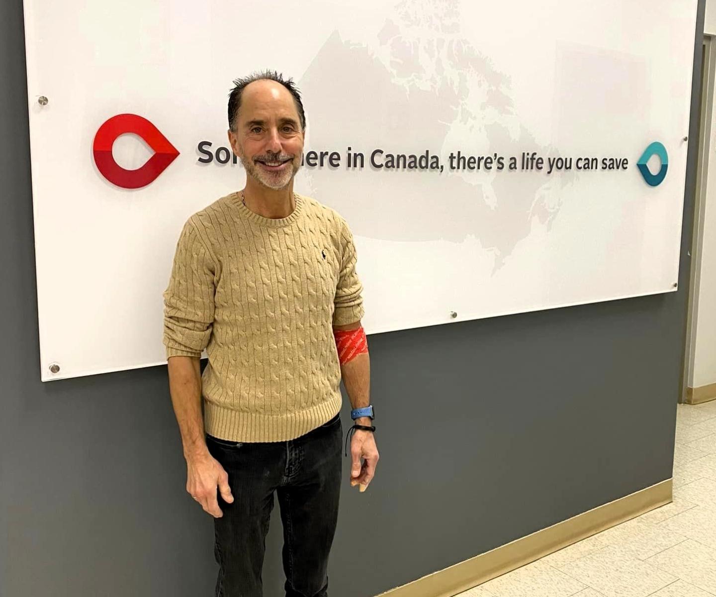 Blood donor in front of sign that says Somewhere in Canada there's a life you can save