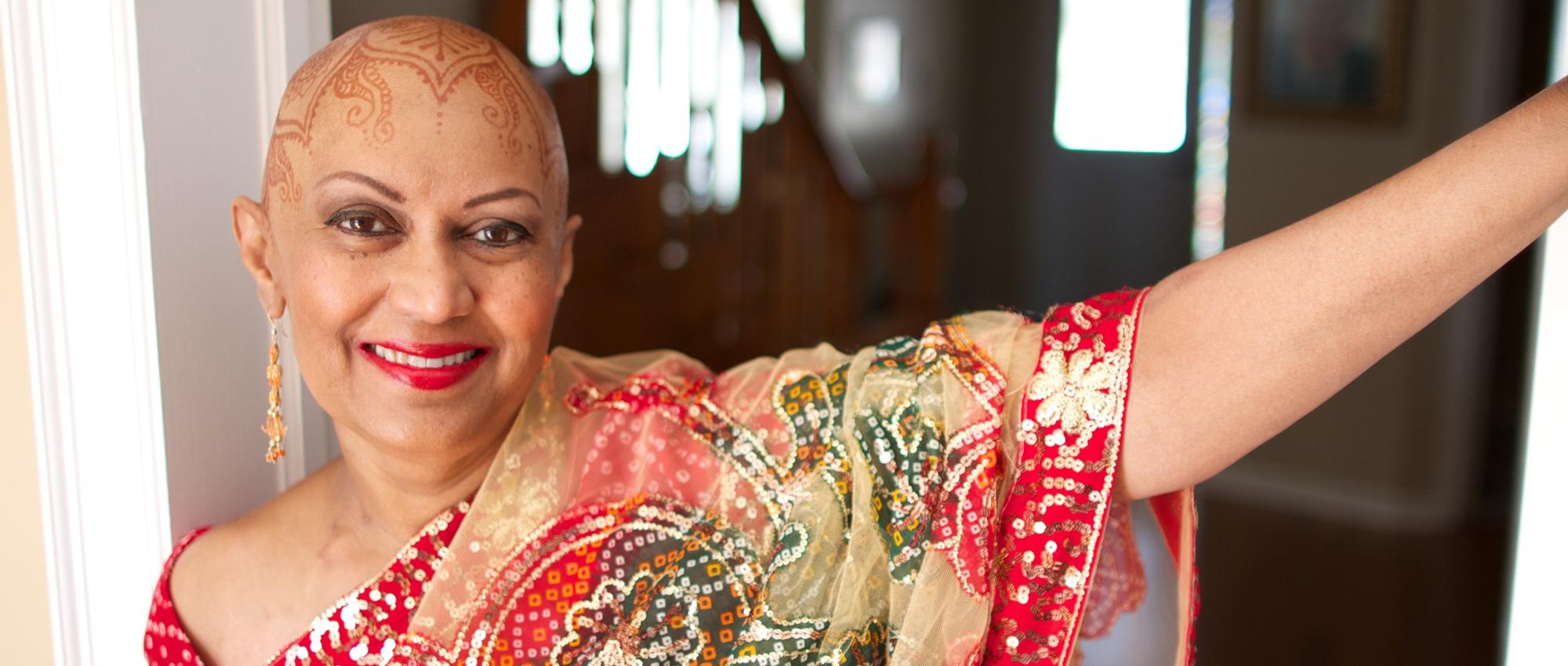 A woman who had blood transfusion procedures during treatment for three different types of cancer stands in a doorway. Her head is painted with a henna design.